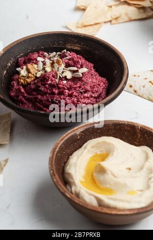 Healthy snack, gourmet dips. Beetroot hummus with walnuts, sunflower seeds on top, chickpeas hummus in ceramic bowls, close up Stock Photo