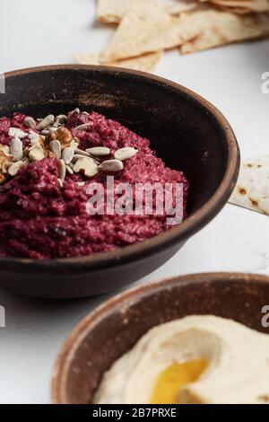 Healthy snack, gourmet dips. Beetroot hummus with walnuts, sunflower seeds on top, chickpeas hummus in ceramic bowls, close up Stock Photo