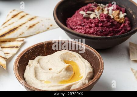 Healthy snack, gourmet dips. Beetroot hummus with walnuts, sunflower seeds on top, chickpeas hummus in ceramic bowls, close up Stock Photo