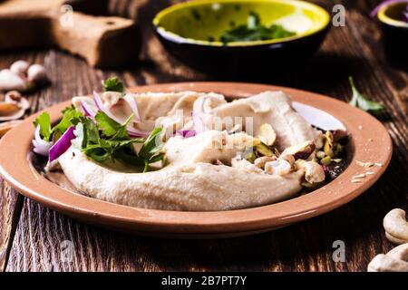 Healthy vegan snack hummus dip with nuts and herbs in ceramic bowl, close up Stock Photo