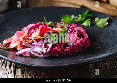 Beetroot horseradish  hummus with pickled watermelon radishes on rustic wooden table, plant based food, close up Stock Photo