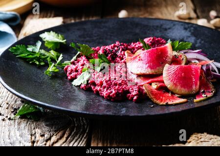 Beetroot horseradish  hummus with pickled watermelon radishes on rustic wooden table, plant based food, close up Stock Photo