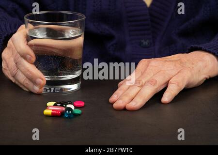 Close up picture of elderly female hands taking medication, dark backgrund Stock Photo