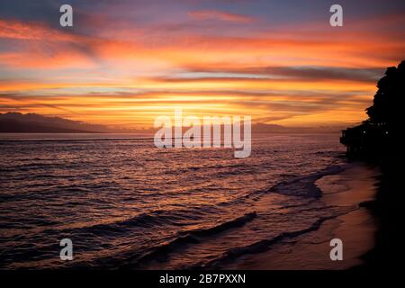 Sunset over the ocean with bright colors of orange and purple reflecting on surface of sea. Stock Photo