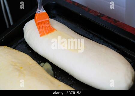 Orange culinary brush on raw dough. The process of lubricating a yeast dough with a beaten egg. Silicone brush cooking home baking. Stock Photo