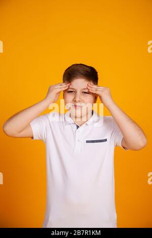 A boy with a headache. Caucasian child on a yellow background suffering from headache and migraine. Hands on the head. Stock Photo