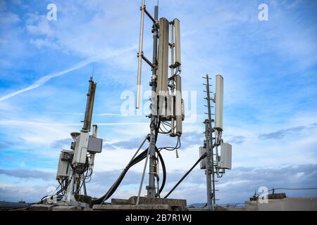 Cellular radio telecommunication network antenna mounted on a metal pole providing strong signal waves from the top of the roof across big city Stock Photo