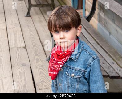 Adorable, blue eyed little boy with a cute pout, dressed in a western style outfit with a red bandana and blue jeans. Stock Photo