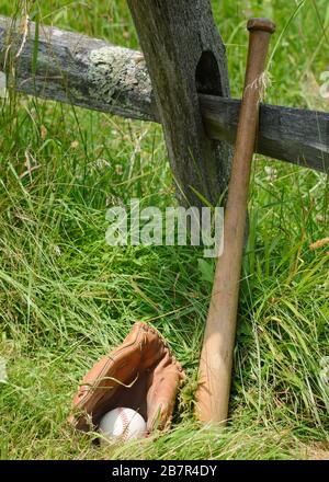 Baseball glove with ball inside and a bat leaning against a an old post. Stock Photo