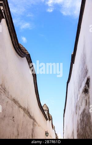 Looking skyward in a hutong alley between two white traditional brick concrete walls and tiles,which is the typical architectural style of Ming and Qi
