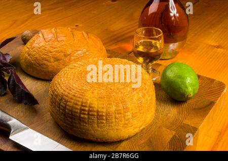 national Adyghe cheese homemade on a cutting Board with a knife, Basil, parsley, lime, sesame oil, chili pepper, macadamia nuts and a decanter on a Stock Photo