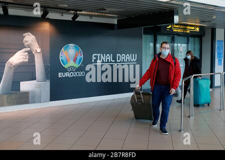 (200318) -- BUCHAREST, March 18, 2020 (Xinhua) -- People wearing face masks pass a logo of the EURO 2020 European Football Championship displayed on a wall at Henri Coanda International Airport in Bucharest, Romania, March 17, 2020. The European football governing body UEFA has decided to postpone this summer's European Championship to 2021 due to the coronavirus outbreak. Romanian President Klaus Iohannis announced that the country will enter an emergency state starting March 16, in an effort to ensure that the government uses all resources to fight the COVID-19 epidemic. (Photo by Cristian Stock Photo