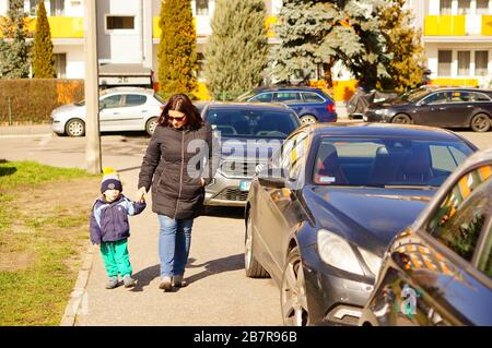 POZNAN, POLAND - Mar 08, 2020: Woman and child holding hands while walking on a sidewalk with parked cars. Stock Photo