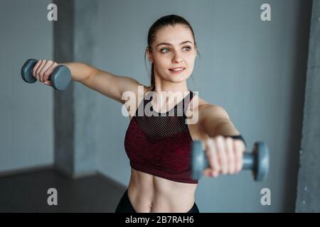 Attractive fit young woman in sport wear smiling girl trains with dumbbells at the loft studio Stock Photo