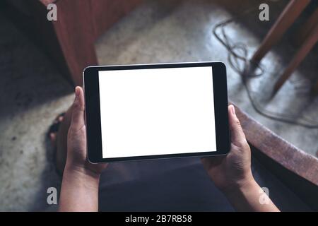 Top view mockup image of a woman sitting and holding black tablet pc with blank white desktop screen Stock Photo