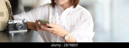 Close up view of young female photographer using smartphone while waiting for customer Stock Photo