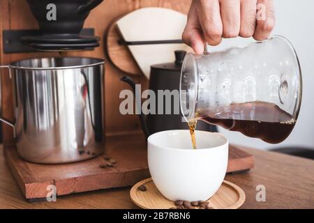 Closeup image of a hand pouring drip coffee into a white mug on vintage wooden table Stock Photo
