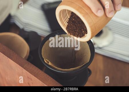 Closeup image of a hand pouring coffee from wooden grinder into a drip coffee filter Stock Photo