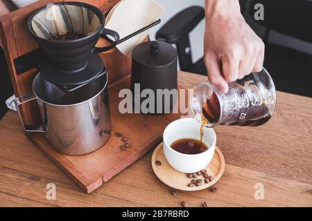 Closeup image of a hand pouring drip coffee into a white mug on vintage wooden table Stock Photo