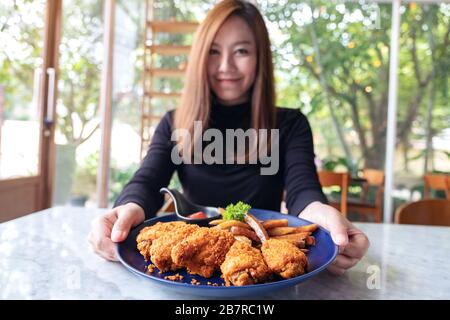 Closeup image of a beautiful asian woman holding and showing a plate of fried chicken and french fries in restaurant Stock Photo