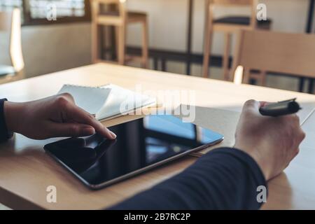 Closeup image of hands pointing at a black tablet pc screen while writing on notebooks in office Stock Photo