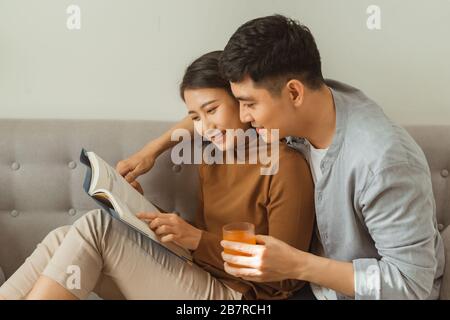 A young, attractive couple is seated together on a couch and are reading a tablet together. Stock Photo
