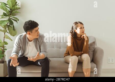 Upset couple at home. Handsome man and beautiful young woman are having quarrel. Sitting on sofa together. Family problems. Stock Photo