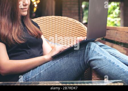 Closeup image of an asian woman using and typing on laptop keyboard while sitting outdoor with feeling relaxed Stock Photo