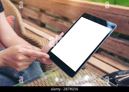 Mockup image of a woman holding and pointing at a black tablet pc with blank white screen while sitting in the outdoors Stock Photo