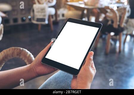 Mockup image of a woman holding black tablet pc with blank white screen while sitting in cafe Stock Photo