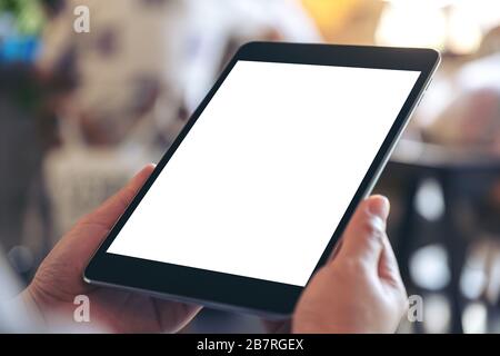 Mockup image of a woman holding black tablet pc with blank white screen while sitting in cafe Stock Photo
