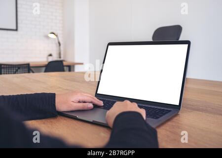 Mockup image of hands using and typing on laptop with blank white desktop screen on wooden table in office Stock Photo