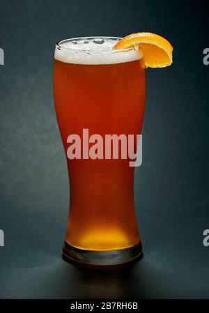 Glass of red beer with orange slice over black background. Beer is one of the oldest, most popular and widely consumed alcoholic drink in the world. Stock Photo