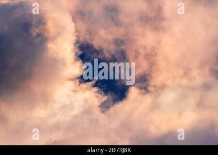 Close up of storm clouds colored in sunset colors; break in the clouds reveals dark blue sky Stock Photo