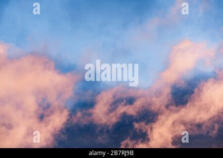 Close up of a layer of clouds colored in sunset colors moving across a bright blue sky Stock Photo