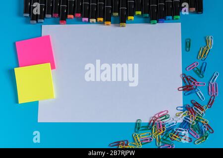 Multi-colored markers, paper clips, stickers and paper on a blue background. Drawing and creativity. Stock Photo