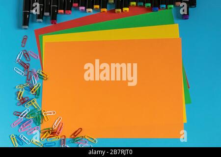 Multi-colored markers, paper clips, stickers and paper on a blue background. Drawing and creativity. Stock Photo