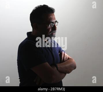 A Indian man with a goatee in a studio against a white background. Wearing spectacles and looking away from camera. Stock Photo