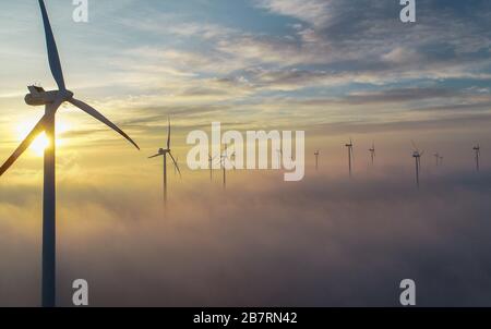 Sieversdorf, Germany. 18th Mar, 2020. The sunset glows brightly over wafts of mist behind wind turbines in the 'Odervorland' wind farm in the Oder-Spree district. There are currently around 3820 wind turbines with a capacity of 7100 megawatts in the state of Brandenburg. Credit: Patrick Pleul/dpa-Zentralbild/ZB/dpa/Alamy Live News Stock Photo