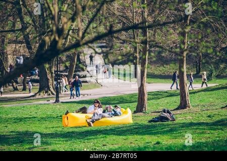 couple laying on yellow inflatable mattress in city park. reading book. drinking smoothies Stock Photo