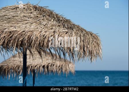 Close Up of parts of Straw Sun Umbrellas on Beach in Santorini in the Greek islands of Greece with blue water behind on empty beach wiht no tourists Stock Photo