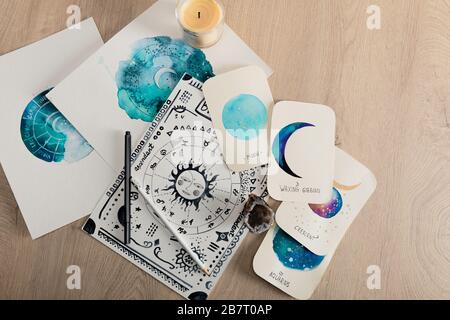 Top view of candle and cards with watercolor drawings of moon phases and zodiac signs on table Stock Photo