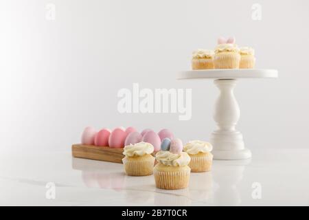 Selective focus of delicious Easter cupcakes on surface and cake stand and painted chicken eggs on grey background Stock Photo