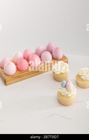 Easter eggs on egg tray with tasty cupcakes on grey background Stock Photo