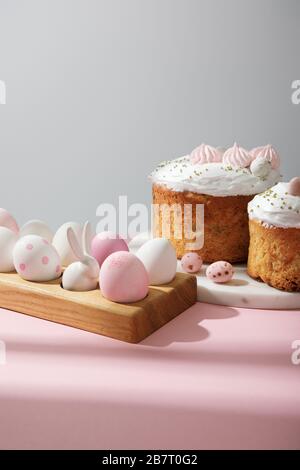 Easter eggs on wooden board with decorative rabbit with easter cakes on pink and grey Stock Photo
