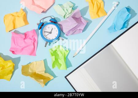 top view of classic alarm clock with blank netbook and pencil on blue background with crumpled colorful sticky notes Stock Photo