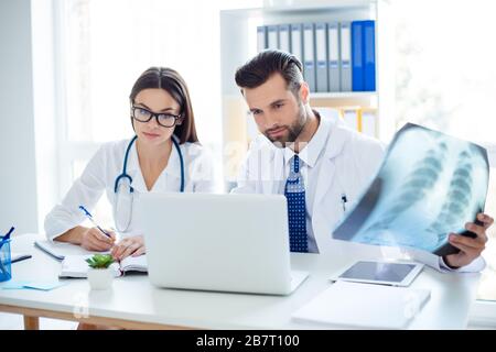 Doctors workers analyzing the x-ray of the patient and checking the results from the laptop while having a meeting Stock Photo