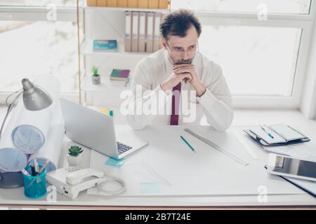 Thoughtful businessman in formal clothes sitting at the table at his office and thinking how to increase profit from new business project Stock Photo