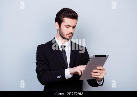 Young serious smart guy in formal clothes holding digital tablet and reading useful information from it Stock Photo