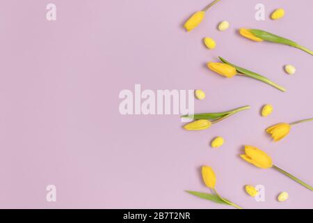 Border frame made of flowers and easter eggs on a purple pastel background. Holiday creative concept. Stock Photo